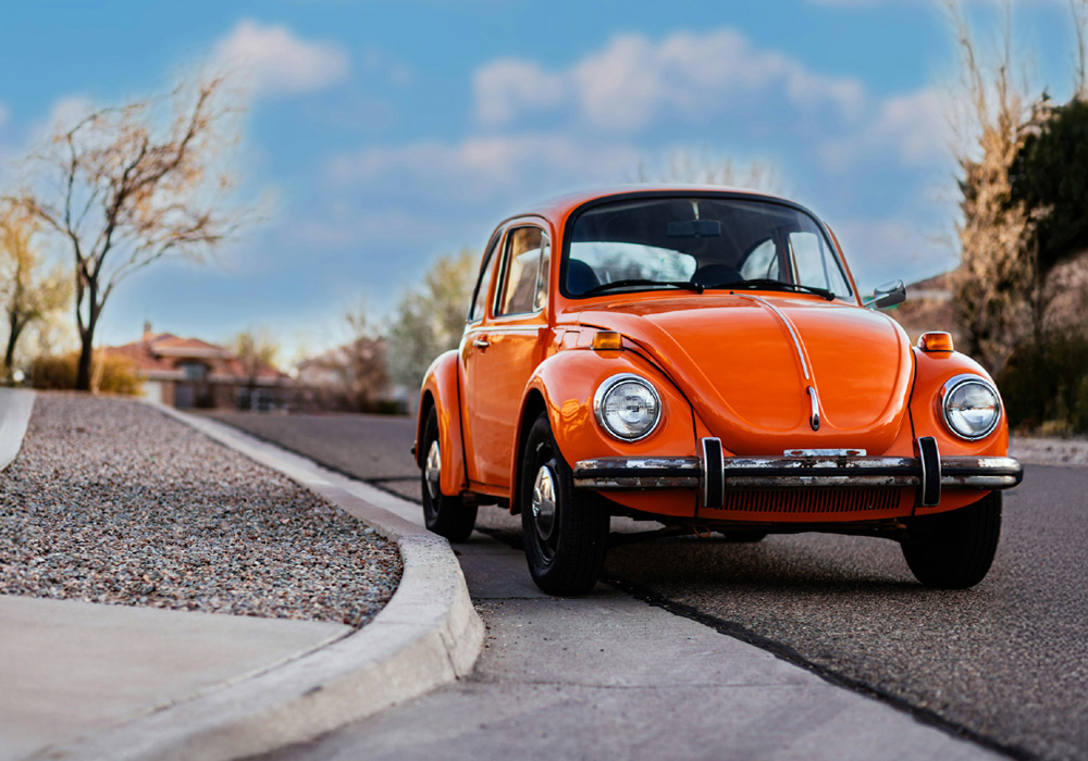 Bright orange Volkswagen Super Beetle parked on a scenic road